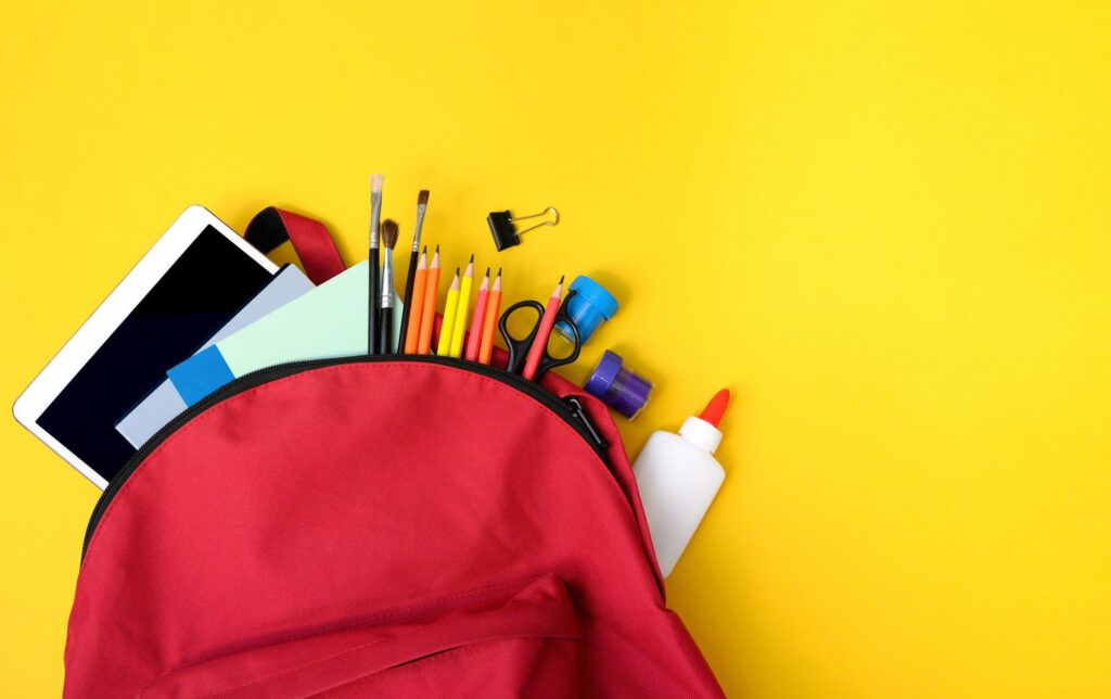 Red Backpack Full of School Supplies on Yellow Background Flat Lay.
