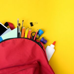 Red Backpack Full of School Supplies on Yellow Background Flat Lay.