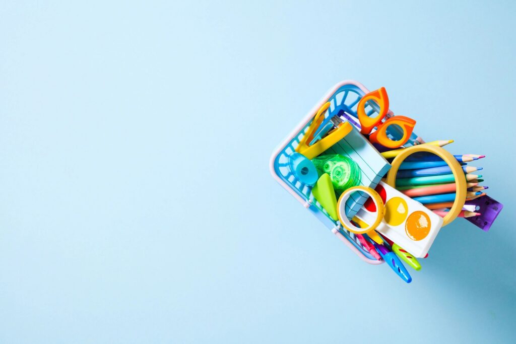 Back to School Concept: A shopping basket filled with colorful school and art supplies on a light blue background with copy space.