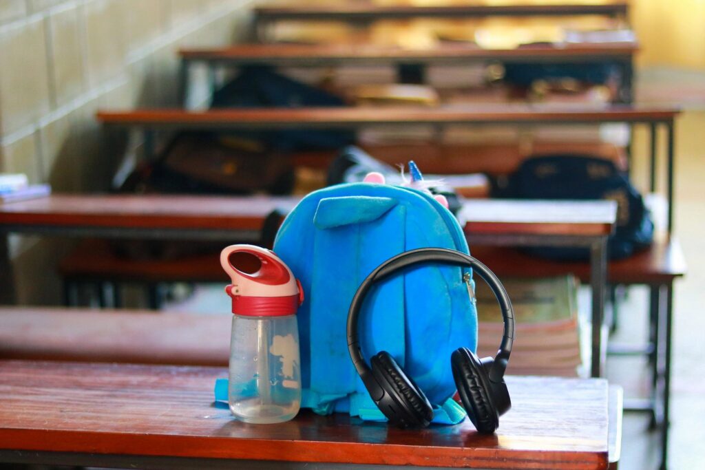 Student Essentials Concept with Blue Backpack, Black Headphones, and Water Bottle on Wooden Table