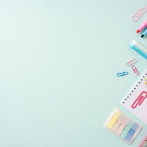 Flat lay of colorful school stationery including scissors, pencils, markers, paper clips, and a notebook on a light blue background